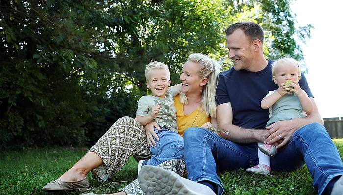 Eltern mit zwei Kindern sitzen auf einer Wiese.